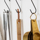 Detachable leather hanging strings by Keyaiira used to hang wooden and metal kitchen utensils on wall hooks — handcrafted leather hanging strings for functional home organization with a white wall behind it.