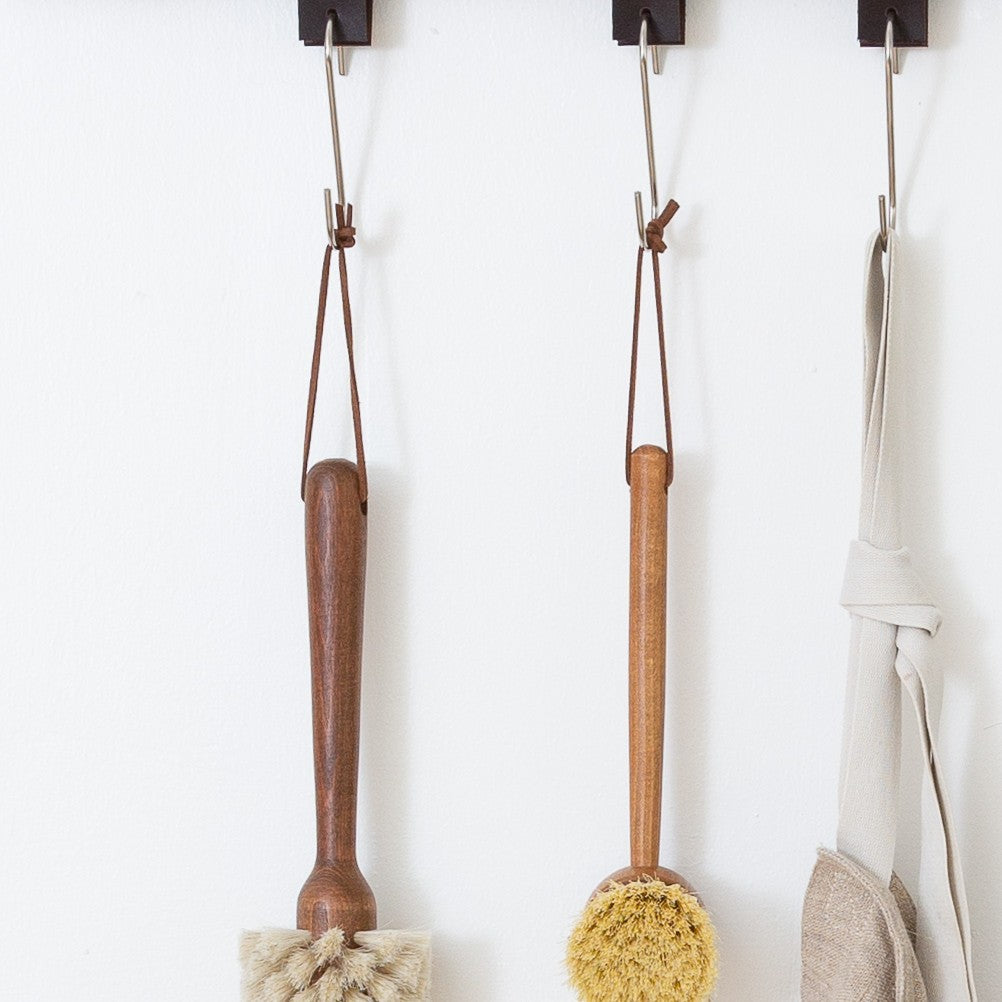 Wooden dish brushes and natural scrubbers hanging from detachable leather hanging strings by Keyaiira — handmade leather hanging strings for sustainable kitchen organization.