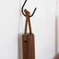 Close-up of a detachable Keyaiira leather hanging loop tied around a wooden kitchen tool handle and hung on a wall hook handcrafted leather loop with brass hardware for kitchen organization.