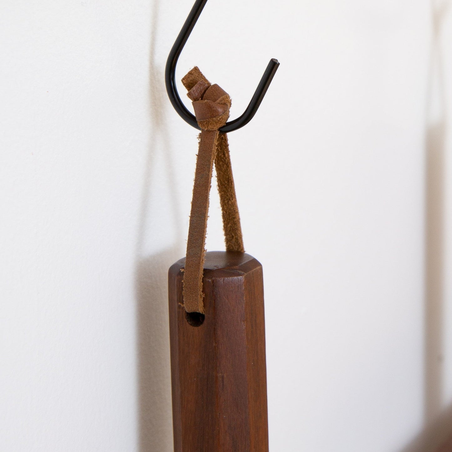 Close-up of a detachable Keyaiira leather hanging loop tied around a wooden kitchen tool handle and hung on a wall hook handcrafted leather loop with brass hardware for kitchen organization.