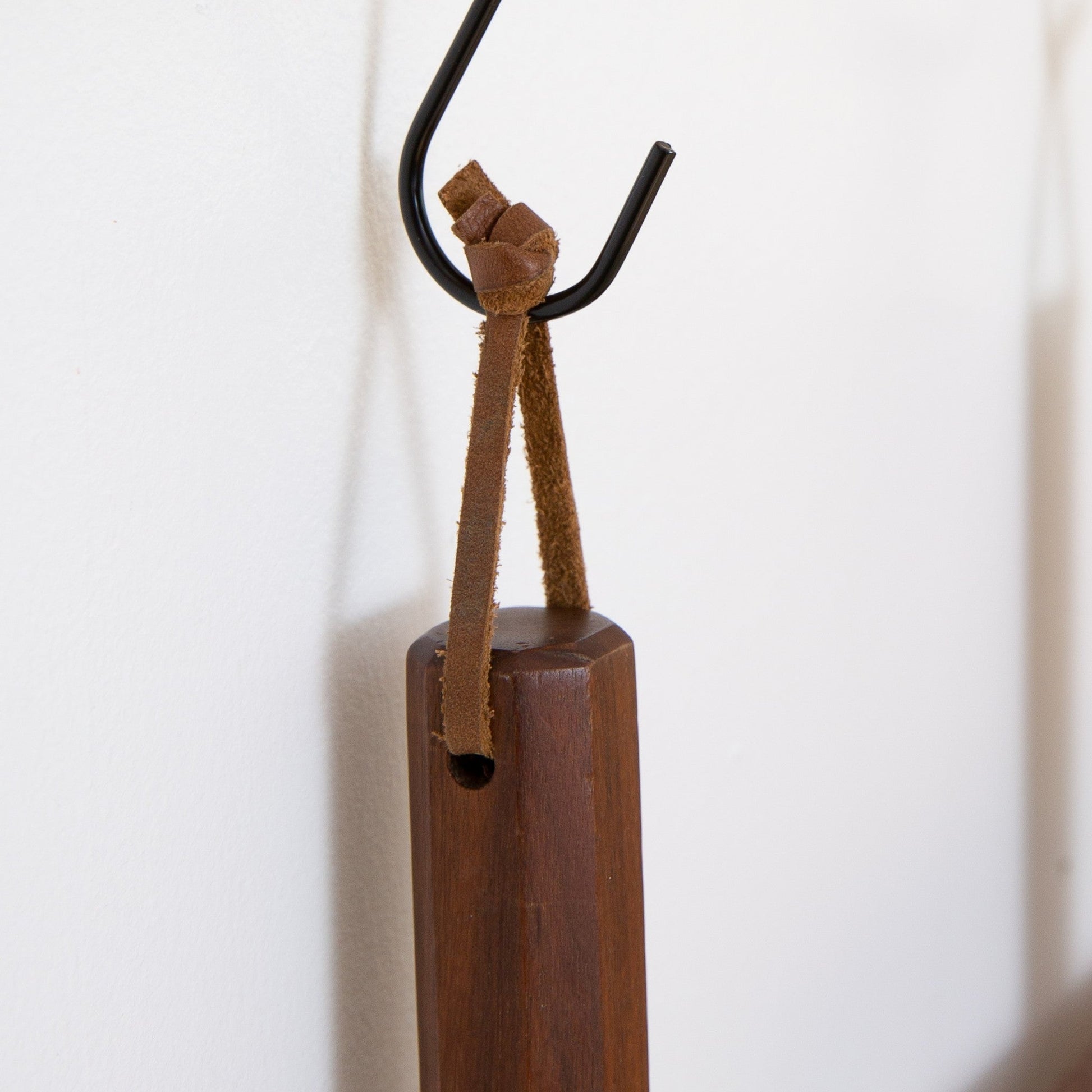 Close-up of a detachable Keyaiira leather hanging loop tied around a wooden kitchen tool handle and hung on a wall hook handcrafted leather loop with brass hardware for kitchen organization.
