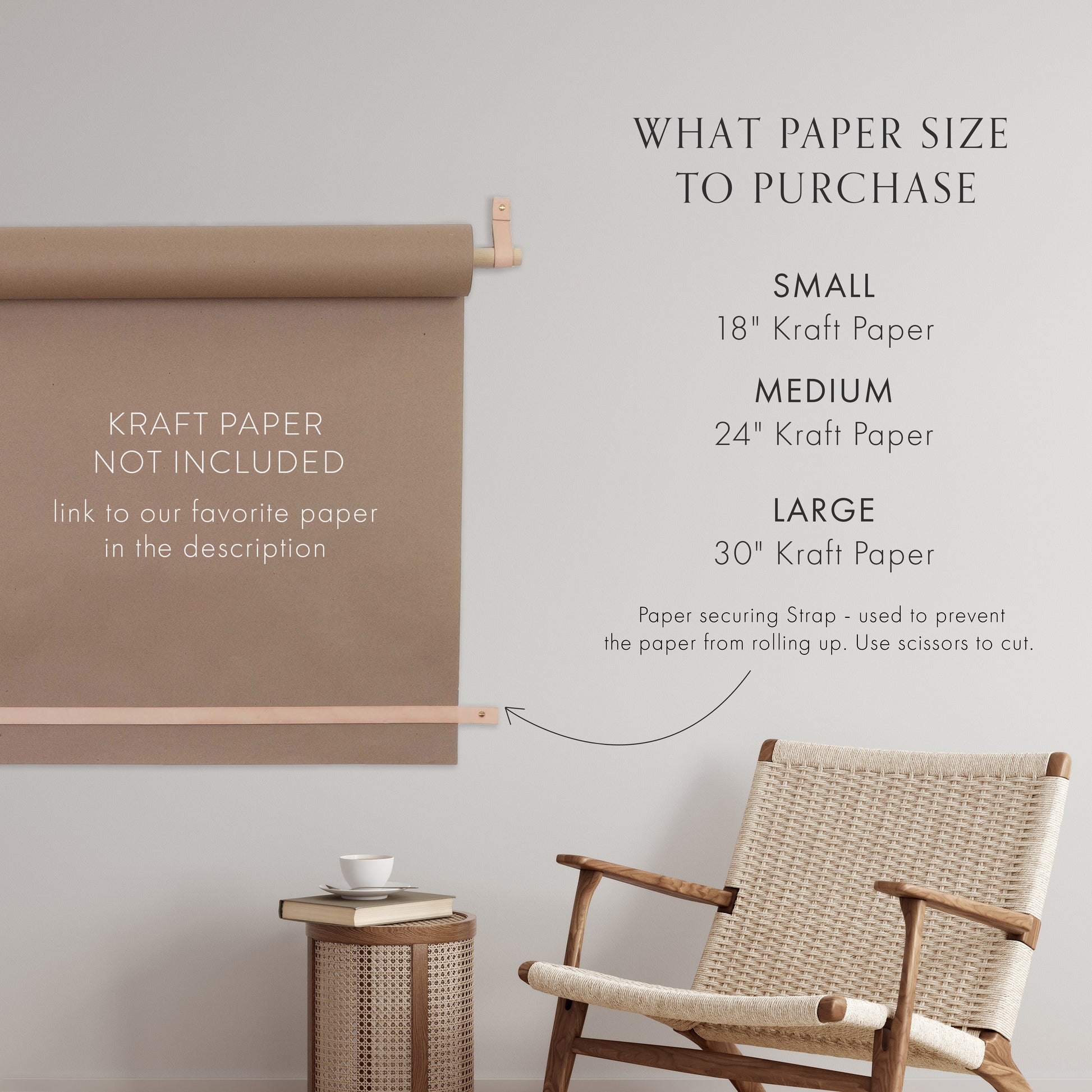 Keyaiira kraft paper holder size guide displayed on a wall, showing recommended paper widths 18-inch small, 24-inch medium, and 30-inch large. Tan leather straps and birch dowel hold a roll of kraft paper above a woven chair, with text noting that kraft paper is not included and a securing strap prevents the paper from rolling up. Modern minimalist décor for home, office, or studio organization.