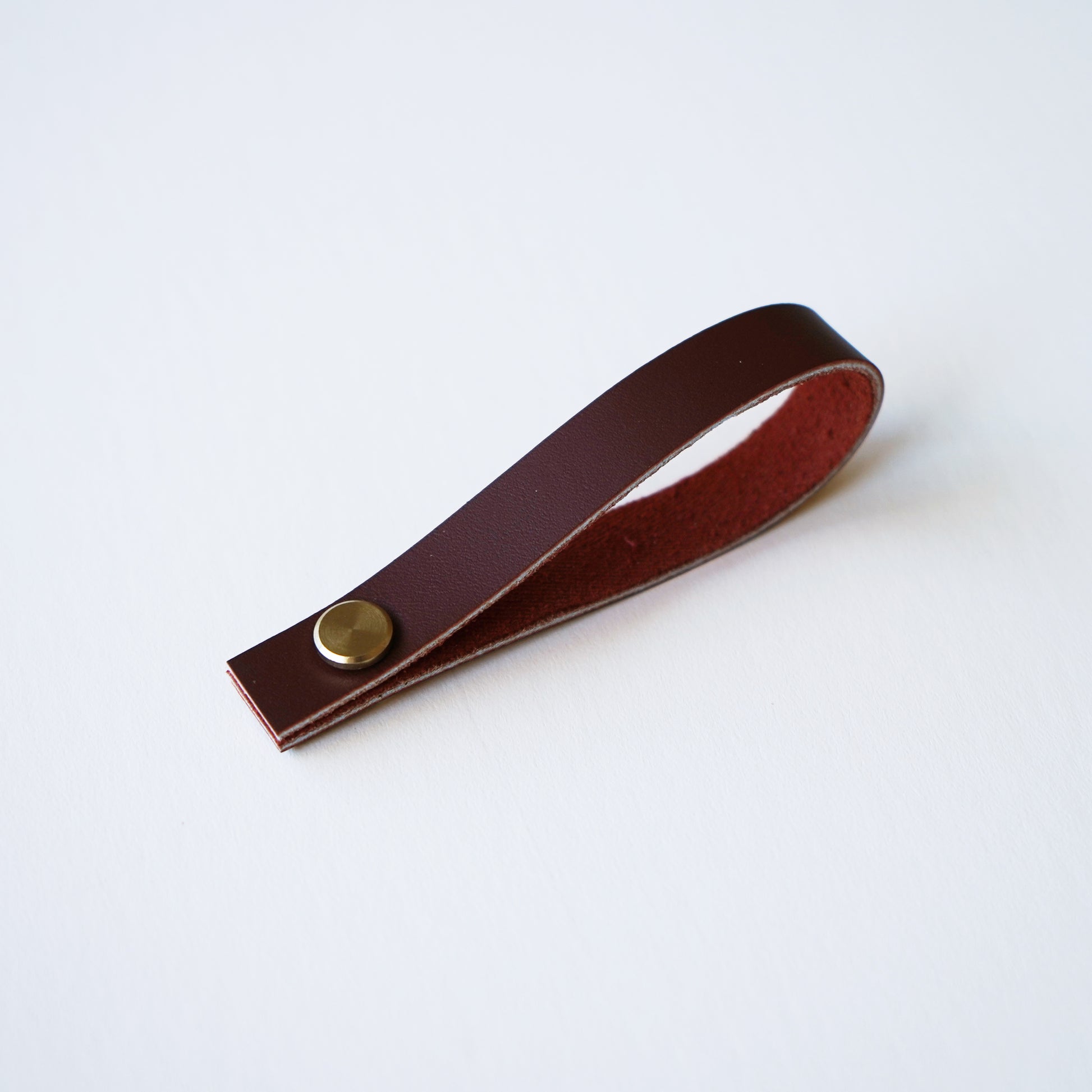Wine colored leather hanging loop with brass hardware on white background minimalist leather hanging loop by Keyaiira.