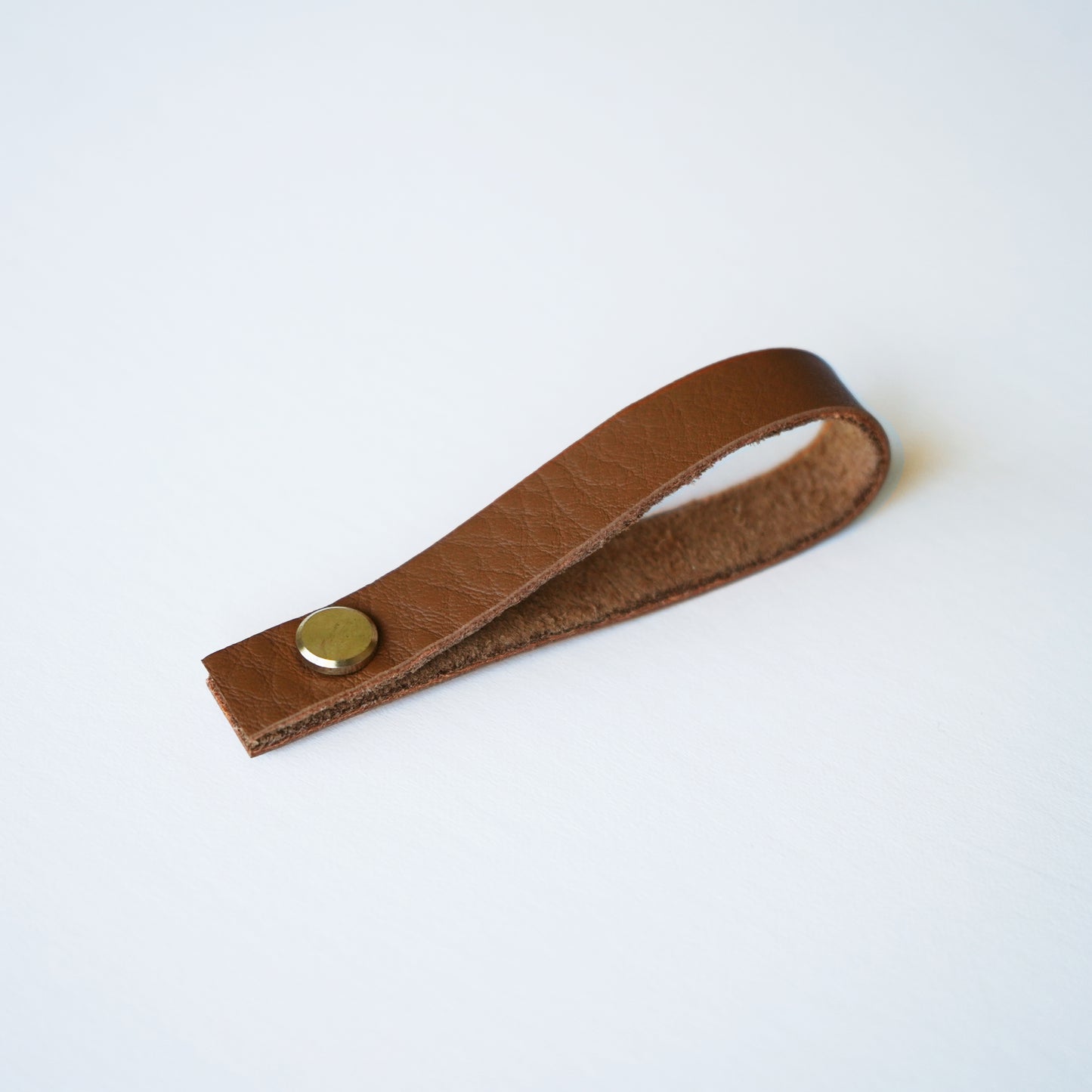 Nicotine colored leather hanging loop with brass hardware on white background — minimalist detachable leather loop by Keyaiira.