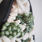 Macro detail shot showing the high contrast between the smooth, rigid brushed black clay and the soft, fuzzy texture of light-colored wools. Highlights the tactile quality of the sustainable materials used in this mixed-media wall sculpture.