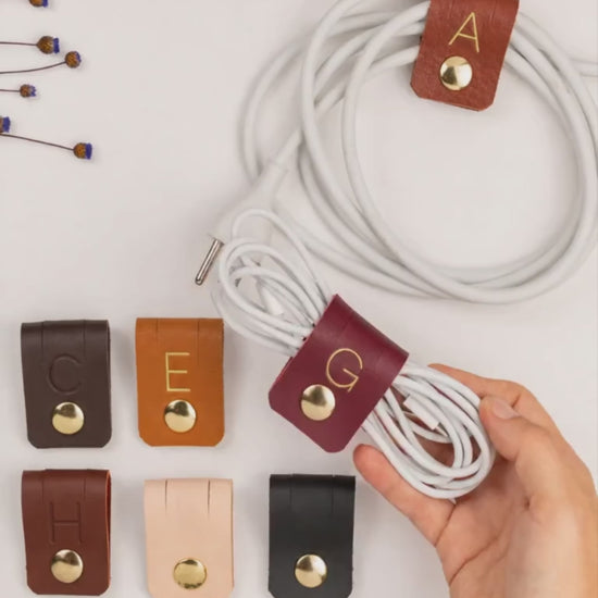 Keyaiira large leather cable holder demonstration showing custom initial options and snap hardware for organizing charging cables, USB cords, power cords and everyday tech accessories
