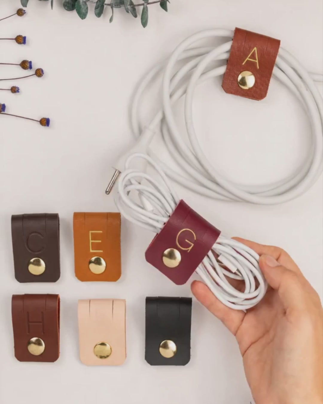 Keyaiira large leather cable holder demonstration showing custom initial options and snap hardware for organizing charging cables, USB cords, power cords and everyday tech accessories
