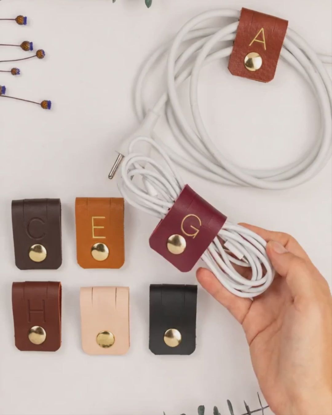 Custom Wine leather G initial cable holder shown with assorted personalized cord organizers, handmade monogram charger ties for electronics storage, desk organization and gifting by Keyaiira
