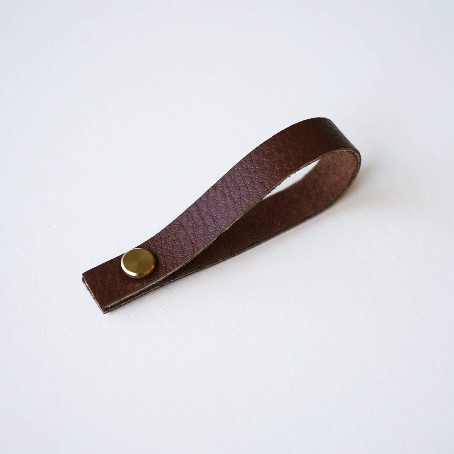 Walnut leather hanging loop with brass fastener on white background Keyaiira leather loop for hanging kitchen textiles.