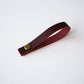 Wine colored leather hanging loop with brass rivet on white background — removable handcrafted leather loop by Keyaiira.