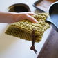 Handwoven cotton potholder with leather cord hanger in olive green — thick textured kitchen hot pad designed for lifting cast iron cookware and protecting countertops.